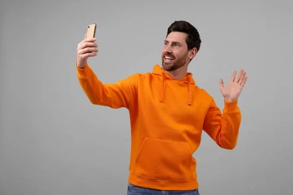 笑的男人拿着智能手机在灰色背景下自拍 — 图库照片