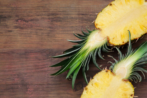Halves of delicious ripe pineapple on wooden table, flat lay. Space for text