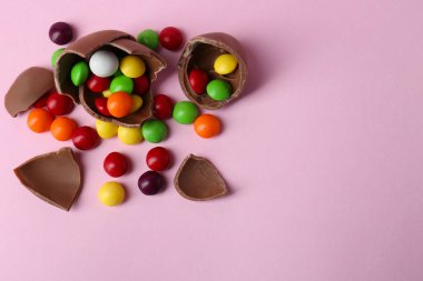 Kırık çikolata yumurtası, pembe arka planda renkli şekerler, düz yatış. Metin için boşluk