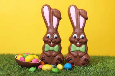 Paskalya kutlaması. Komik çikolatalı tavşanlar ve sarı arka planda küçük şekerli tatlı yumurtalar.