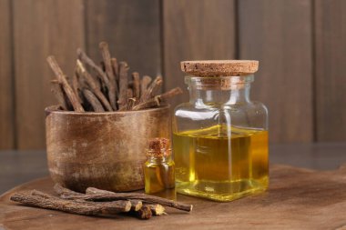 Kurumuş meyan kökü çubukları ve ahşap tahtada gerekli yağ, yakın plan.