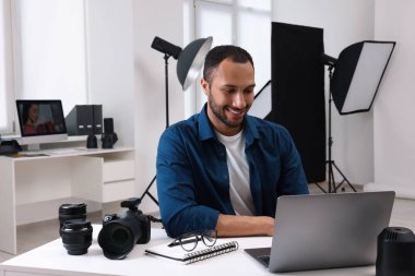 Modern fotoğraf stüdyosunda dizüstü bilgisayarda çalışan genç profesyonel fotoğrafçı.