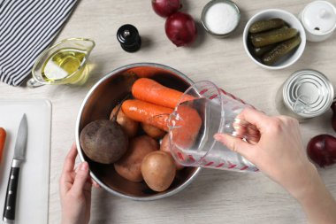 Beyaz ahşap masada taze sebzelerle kaseye su döken kadın. Sirkeli salata pişiriyorum.