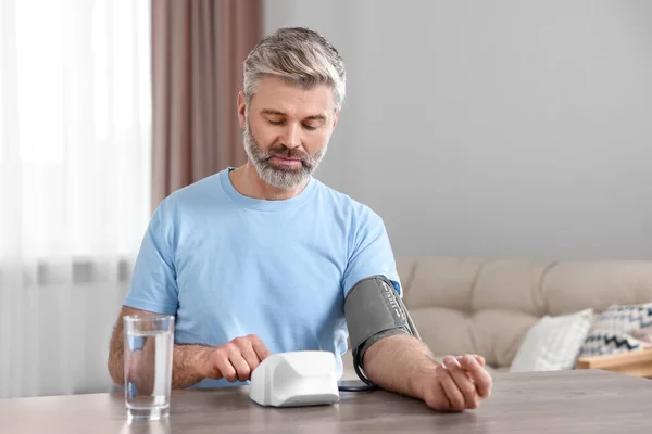 stock image Man measuring blood pressure at table indoors