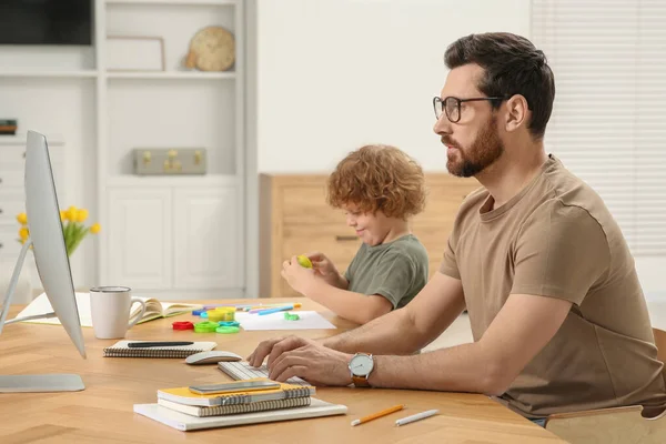 stock image Man working remotely at home. Father using computer while his son playing at desk