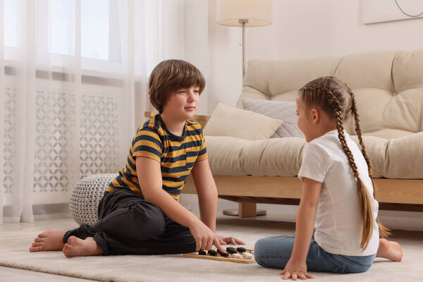 Cute boy playing checkers with little girl on floor in room