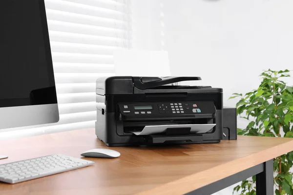 Modern printer with paper near computer on wooden table in home office