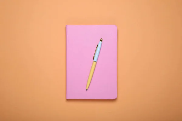 Closed pink office notebook on pale orange background, top view
