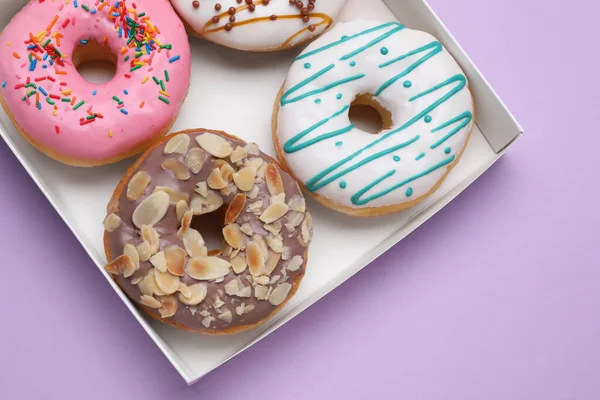 stock image Box with different tasty glazed donuts on violet background, top view