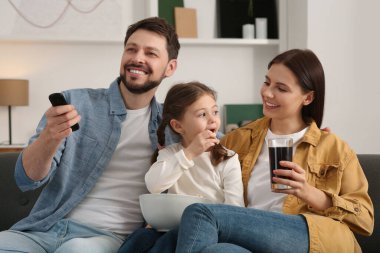 Evde film izleyen mutlu bir aile. Babam uzaktan kumandayla televizyon kanallarını değiştiriyor.
