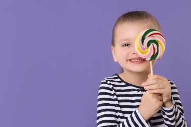 Mor arka planda renkli lolipop kıvrımlarıyla gözlerini kapayan mutlu küçük kız, mesaj için boşluk.