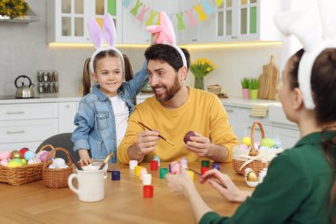 Happy family having fun while painting Easter eggs at table in kitchen