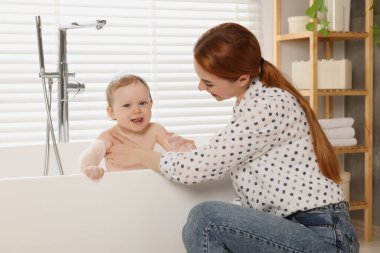 Anne küçük bebeğini küvette yıkıyor.