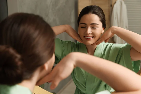 年轻女子在浴室的镜子前按摩她的脸 — 图库照片
