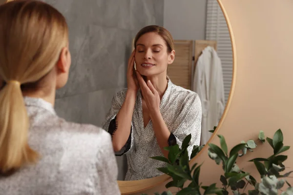 stock image Woman massaging her face near mirror in bathroom