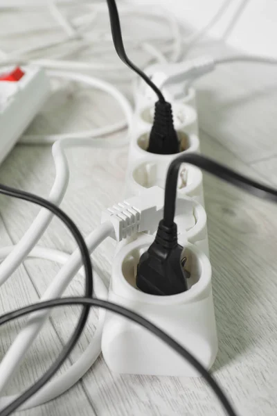 Power strip with different electrical plugs on white floor, closeup