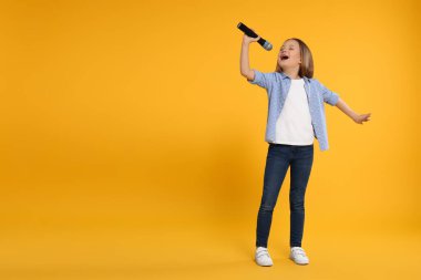 Sarı arka planda mikrofonlu şirin küçük kız şarkı söylüyor.