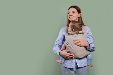 Anne zeytin arka planında çocuğunu askıda (bebek taşıyıcısı) tutuyor