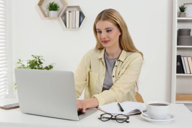 Ev işyerinde. Beyaz masadaki odada dizüstü bilgisayarda çalışan bir kadın.