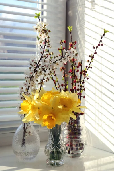 Yellow daffodils and beautiful branches in vases on windowsill