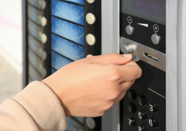 Using coffee vending machine. Woman inserting coin to pay for drink, closeup