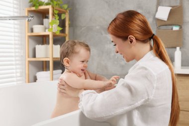 Anne küçük bebeğini küvette yıkıyor.