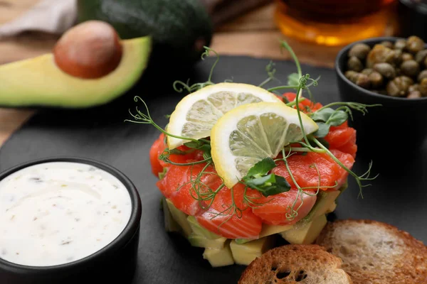 stock image Delicious salmon tartare served with avocado, sauce and croutons on table, closeup