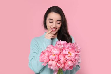 Beautiful young woman with bouquet of peonies on pink background clipart