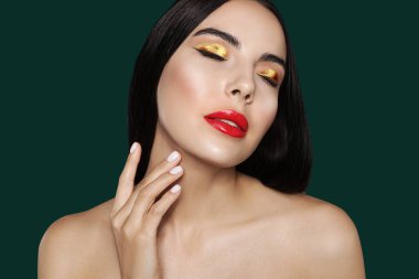 Güzel altın rengi göz farları ve koyu yeşil arka planda kırmızı dudakları olan genç bir kadın.