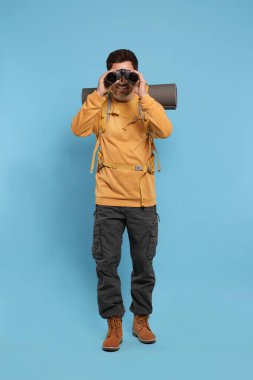 Sırt çantalı bir adam açık mavi arka planda dürbünle bakıyor. Etkin turizm