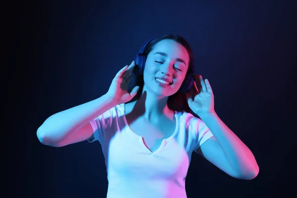 Glückliche Frau Mit Kopfhörern Genießt Musik Neonlicht Vor Dunkelblauem Hintergrund — Stockfoto