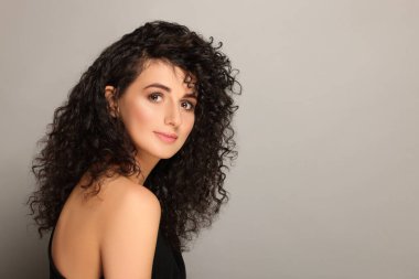 Açık gri arka planda uzun kıvırcık saçlı güzel bir genç kadın. Metin için boşluk