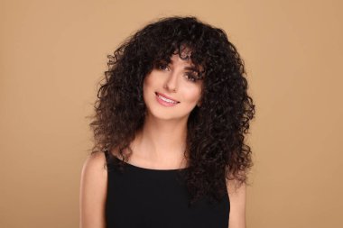 Bej arka planda uzun kıvırcık saçlı güzel bir genç kadın.