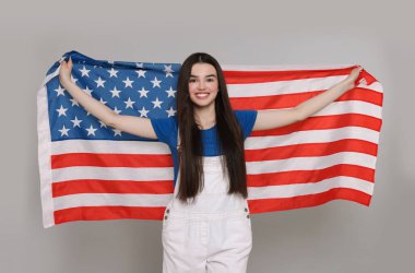 4 Temmuz - ABD 'nin Bağımsızlık Günü. Gri arka planda Amerikan bayrağı taşıyan mutlu kız