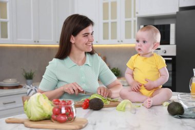 Sevimli bebeğiyle birlikte mutfakta vakit geçiren genç ve mutlu bir kadın.