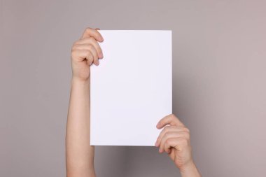 Woman holding sheet of paper on grey background, closeup. Mockup for design