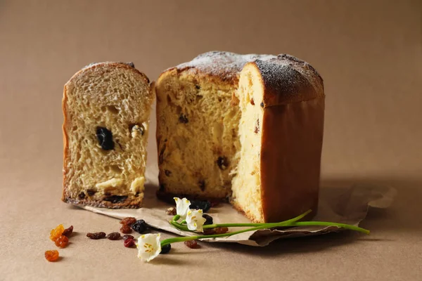 Lezzetli kesilmiş Panettone pastası, kuru üzümler ve açık kahverengi arka planda güzel çiçekler. Geleneksel İtalyan pastası