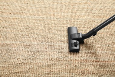 Bej halıyı modern elektrik süpürgesiyle süpürüyor. Metin için boşluk