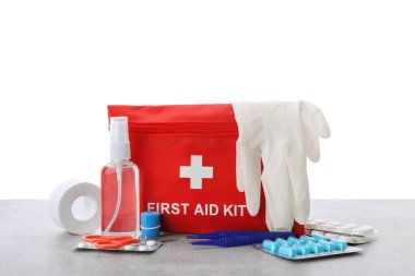 İlk yardım çantası, makas, eldiven, hap, plastik kıskaç ve elastik bandaj açık gri masa üzerinde beyaz arka plan