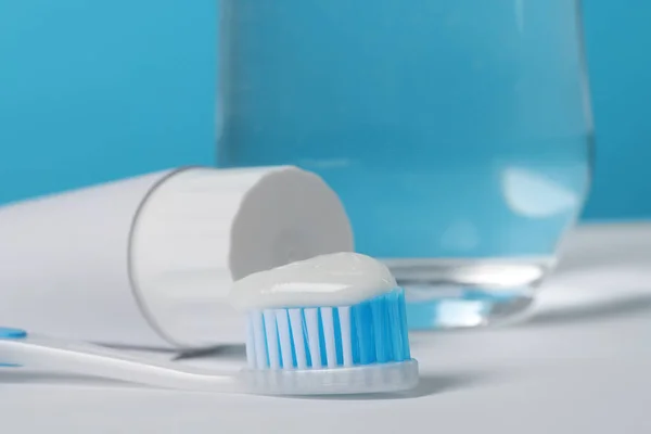 Plastikowa Szczoteczka Zębów Pastą Szklanką Wody Białym Stole Jasnoniebieskim Tle — Zdjęcie stockowe