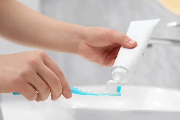 バスルームのシンクの近くの歯ブラシにチューブから歯磨き粉を絞る女性 クローズアップ — ストック写真