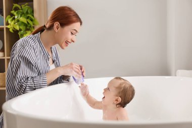 Anne küçük bebeğini küvette yıkıyor.