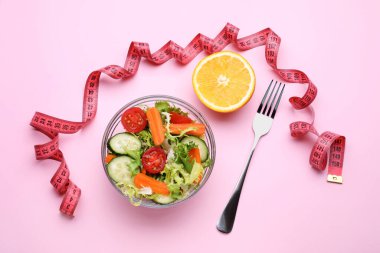 Mezura, salata, turuncunun yarısı ve pembe arka planda çatal, düz yatış.