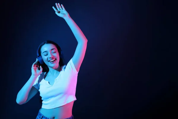 ヘッドフォンで幸せな女性が音楽を聞いて 濃い青の背景にネオンで踊る テキストのスペース — ストック写真