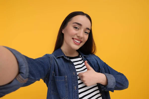 Uśmiechnięta Młoda Kobieta Robi Selfie Pokazuje Kciuki Żółtym Tle — Zdjęcie stockowe