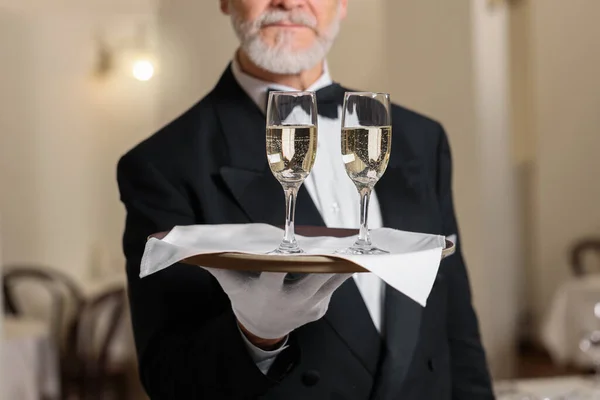 stock image Senior butler holding tray with glasses of sparkling wine in restaurant, closeup