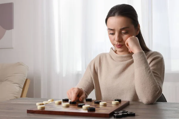 stock image Playing checkers. Concentrated woman thinking about next move at table in room, space for text