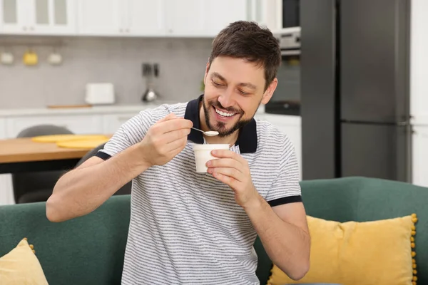 一个英俊的男人在厨房的沙发上吃着美味的酸奶 — 图库照片