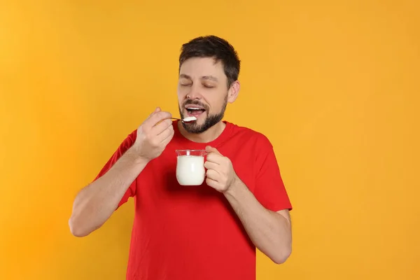 一个英俊的男人在橙色背景下吃着美味的酸奶 — 图库照片