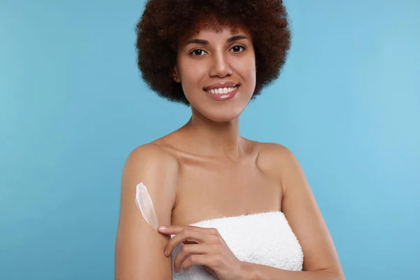 Mooie Jonge Vrouw Aanbrengen Lichaam Crème Arm Licht Blauwe Achtergrond — Stockfoto